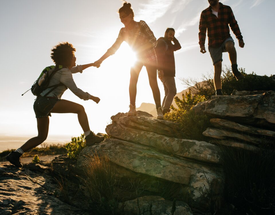 group of hikers on mountain with a women helping her friend climb a rock